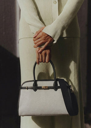 Person holding a gray handbag with a black handle against a neutral background