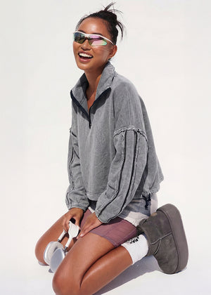 Woman wearing a gray sweatshirt and purple shorts sitting on a white background