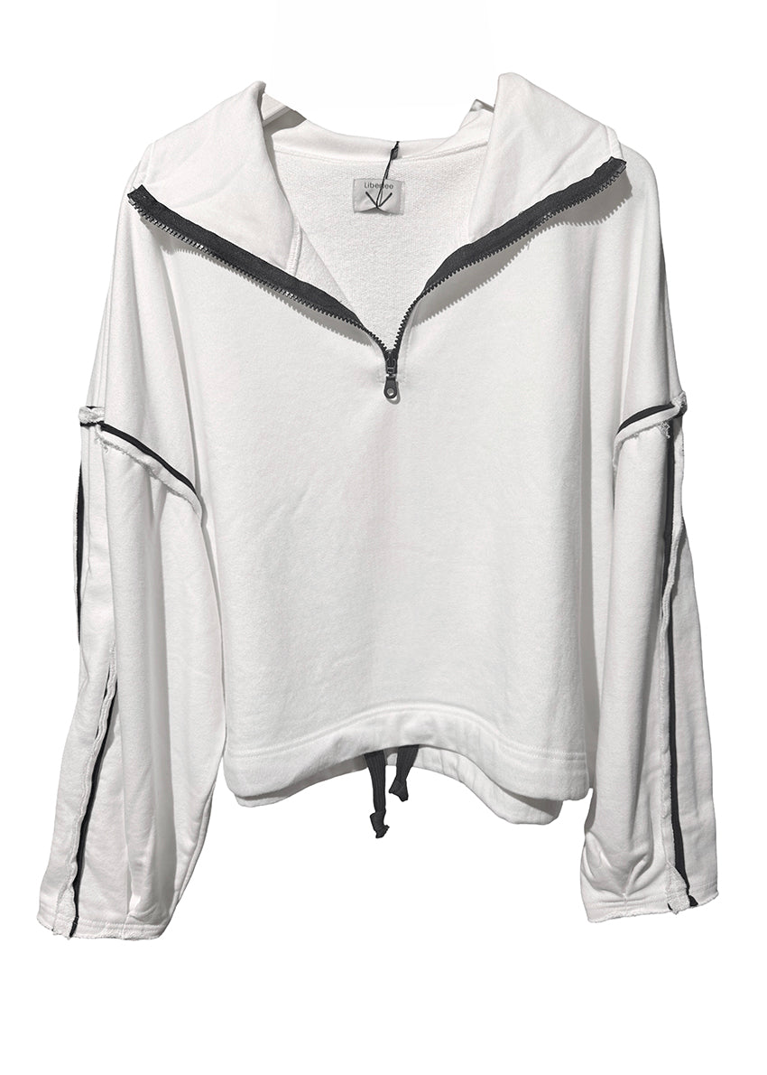 Woman wearing a white sweatshirt and gray shorts with sunglasses and headphones, standing on a white surface.
