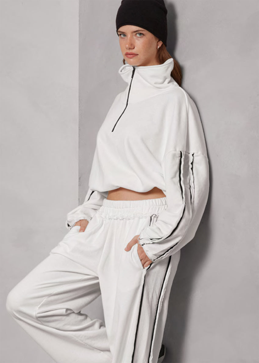 Person wearing a white tracksuit with a black beanie against a gray background