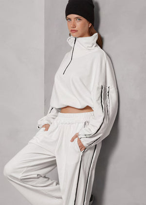 Person wearing a white tracksuit with a black beanie against a gray background