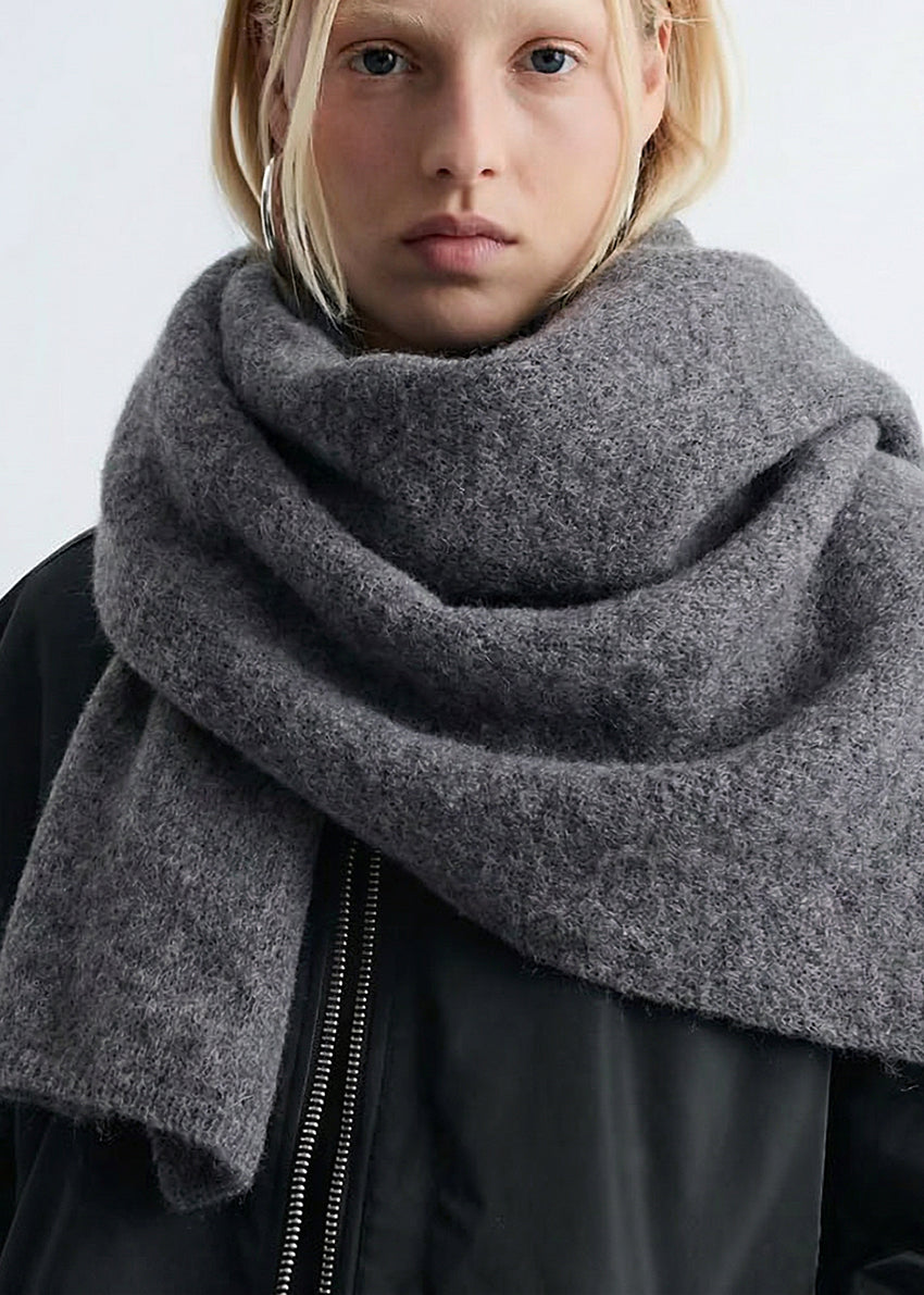 Person wearing a large gray scarf against a white background
