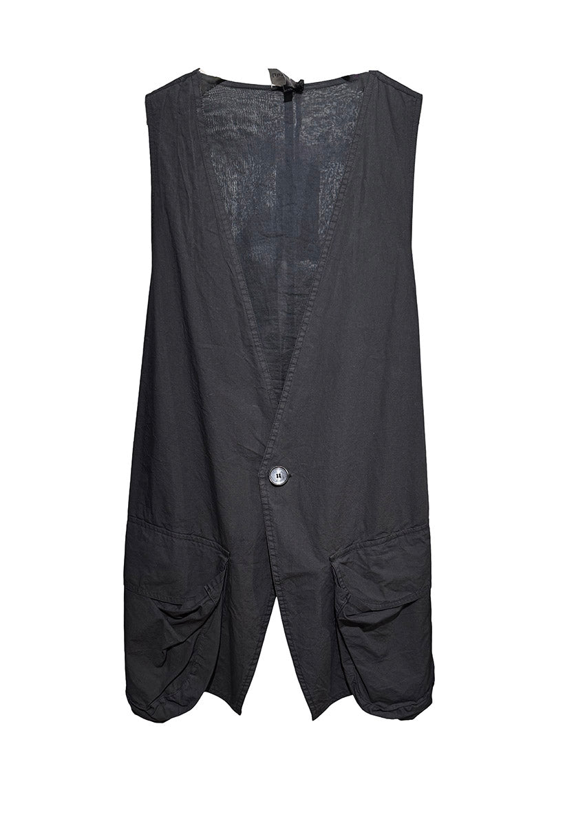 Person wearing a black sleeveless vest, denim shorts, and black boots standing against a black wire fence.