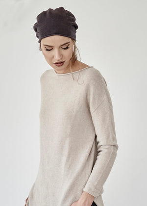 Woman wearing a beige sweater and dark headscarf on a plain background