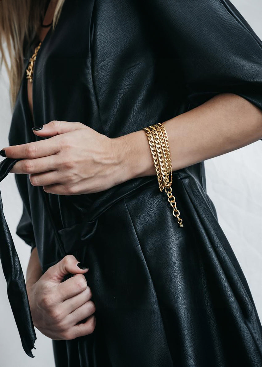 A person wearing a black leather jacket and a silver chunky chain bracelet.