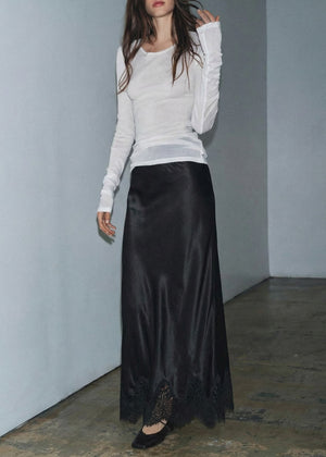 Person wearing a white long-sleeve top and black satin skirt against a plain background