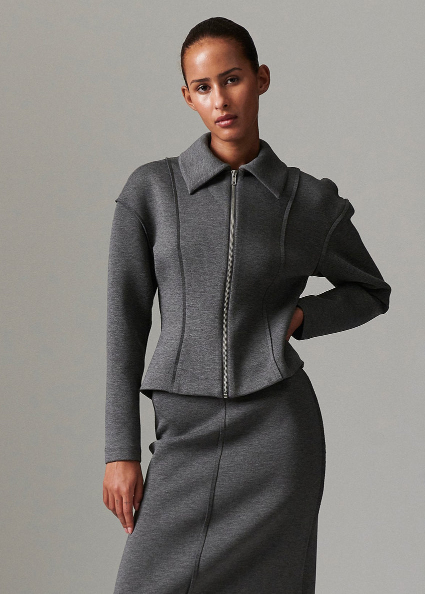 Woman wearing a gray zip-up jacket and skirt against a plain background