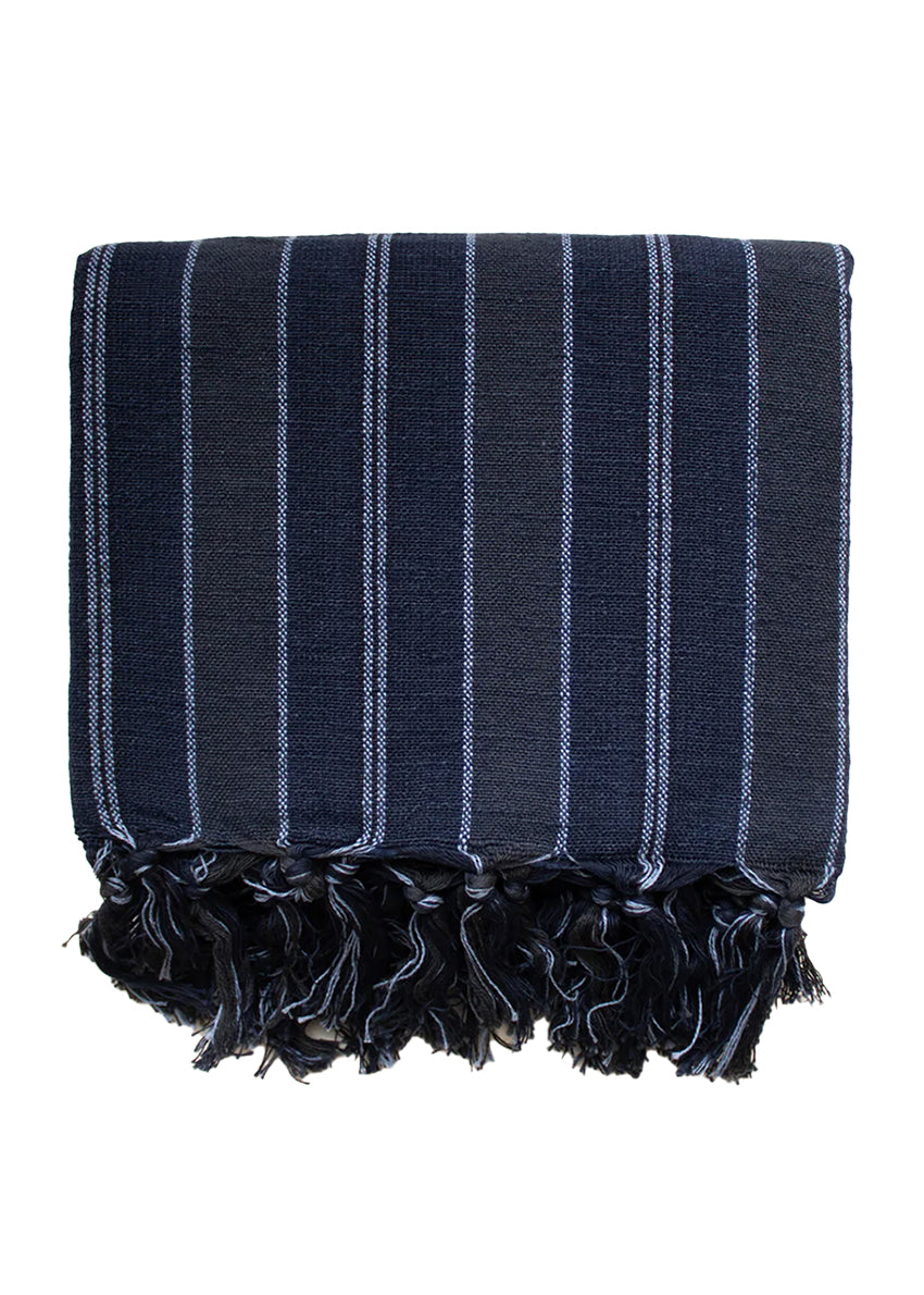 A person standing, wearing a blue striped towel with fringes, sunglasses, and showcasing a smile.