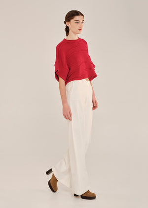 Person wearing a red top and white pants on a plain background