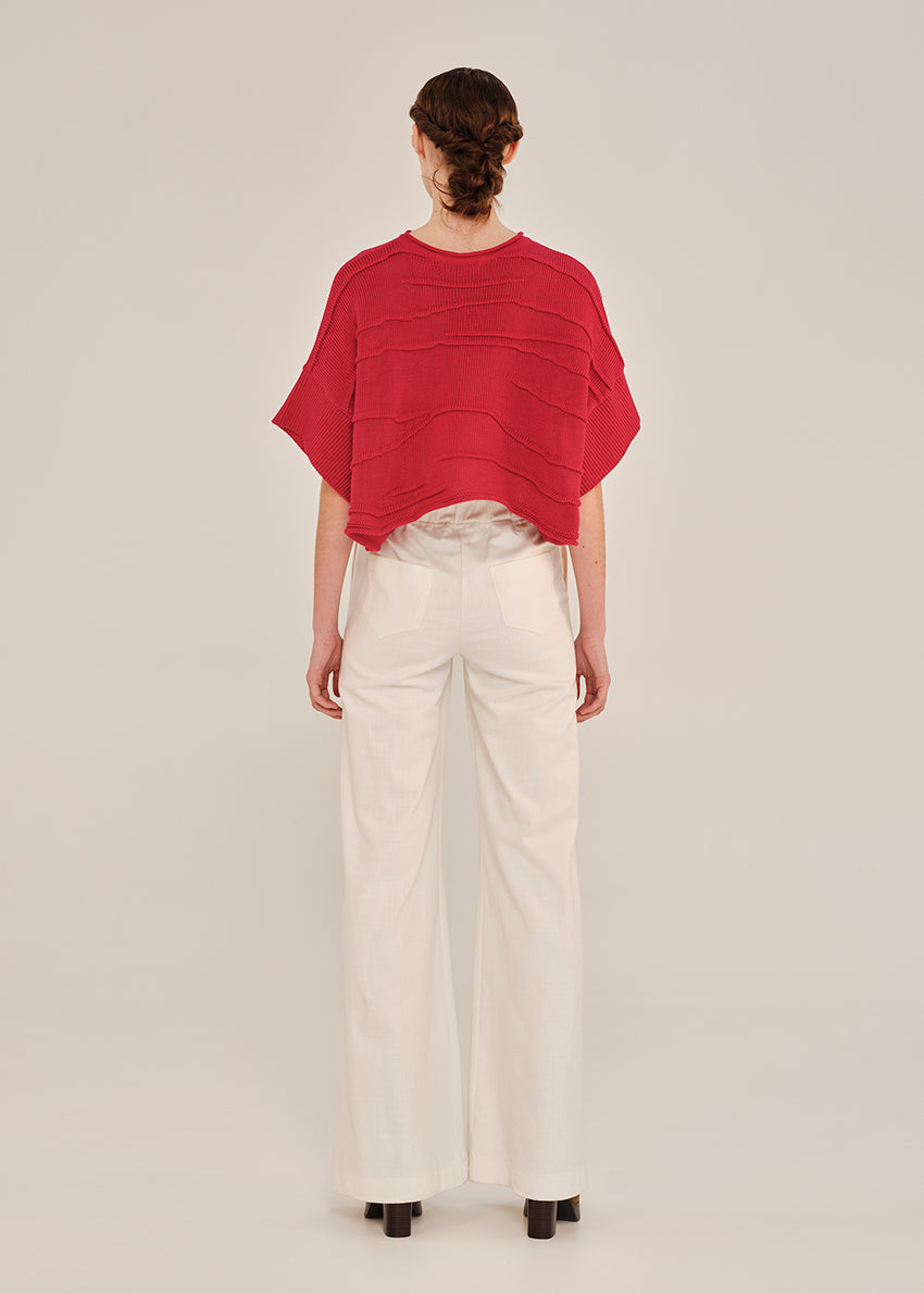 Person wearing a red top and white pants on a plain background