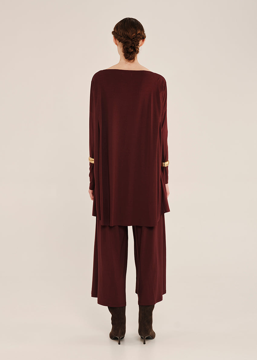 Person wearing a burgundy oversized top with gold accents on a white background