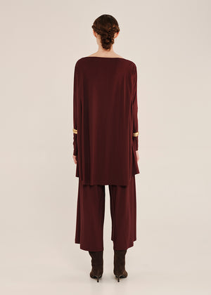 Person wearing a burgundy oversized top with gold accents on a white background
