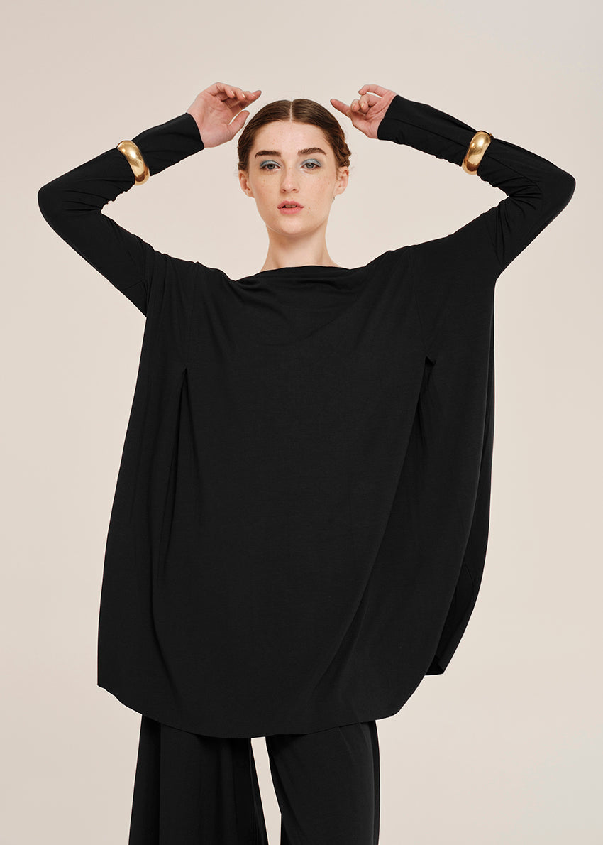 Person wearing a black outfit with gold arm bands on a beige background