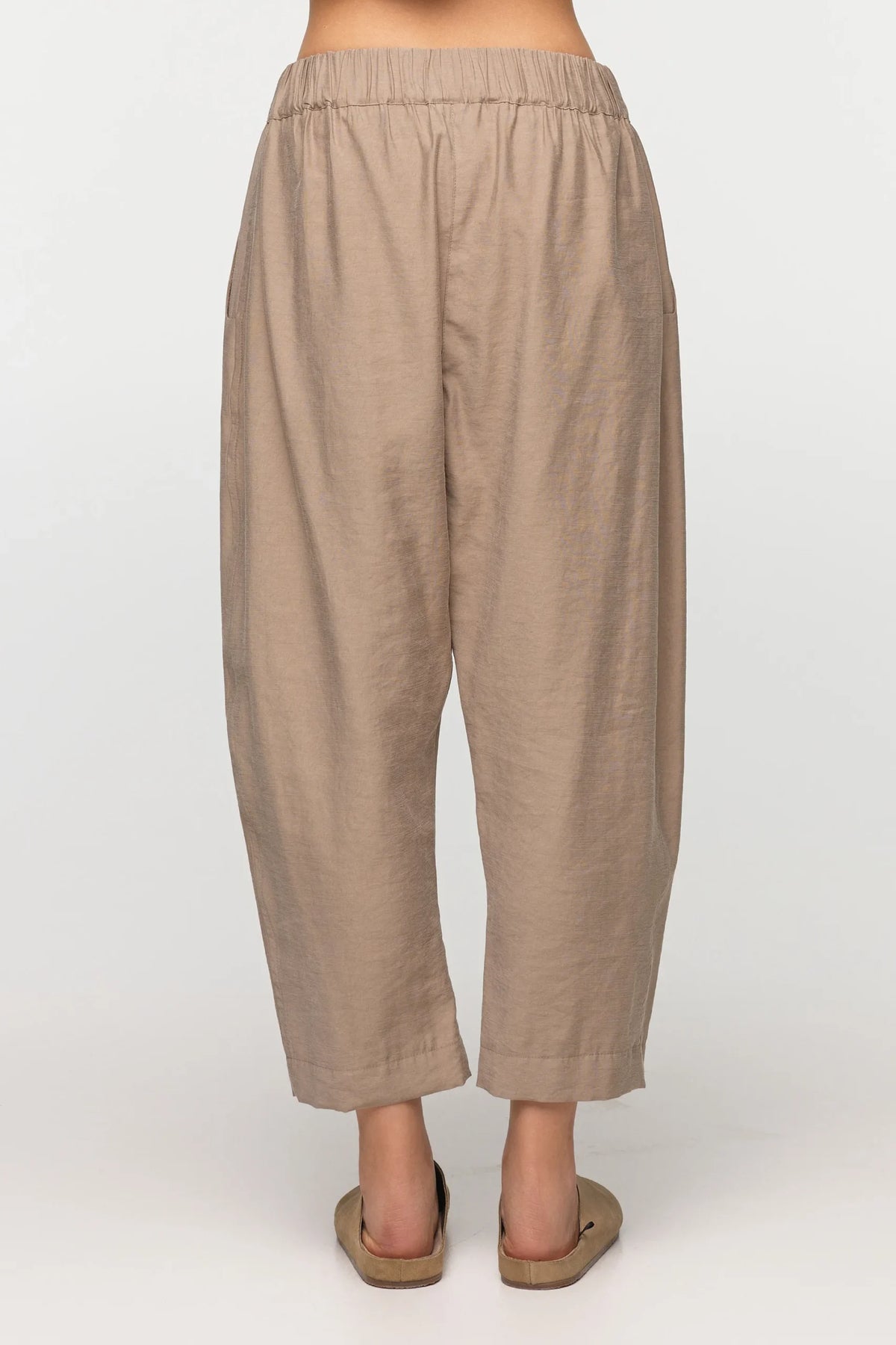 Unisex, mid-length tan trousers, made from soft, non-stretch rayon fabric, in a relaxed, organic cut, featuring a wide elastic waistband, a dropped crotch, and front pockets