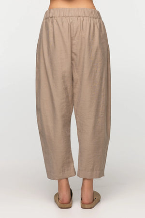 Unisex, mid-length tan trousers, made from soft, non-stretch rayon fabric, in a relaxed, organic cut, featuring a wide elastic waistband, a dropped crotch, and front pockets