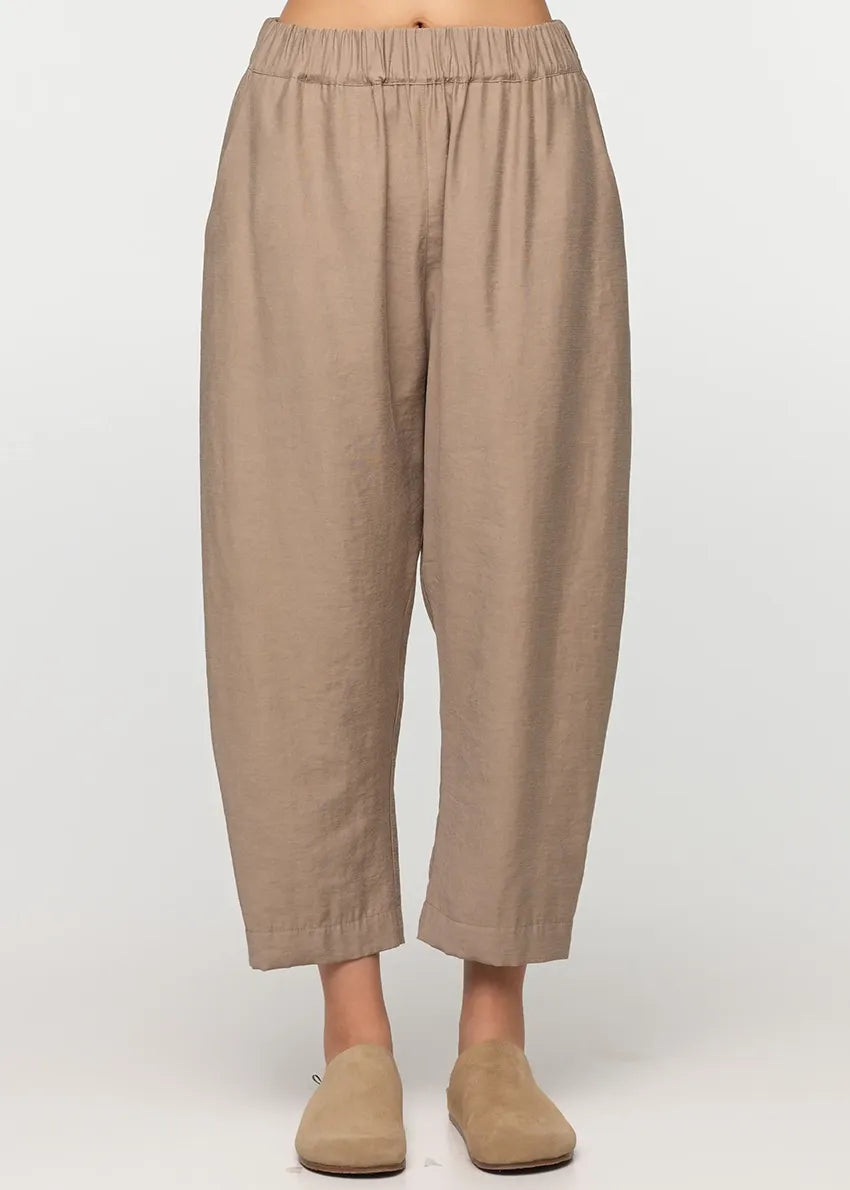 Unisex, mid-length tan trousers, made from soft, non-stretch rayon fabric, in a relaxed, organic cut, featuring a wide elastic waistband, a dropped crotch, and front pockets