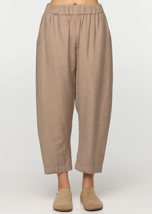 Unisex, mid-length tan trousers, made from soft, non-stretch rayon fabric, in a relaxed, organic cut, featuring a wide elastic waistband, a dropped crotch, and front pockets