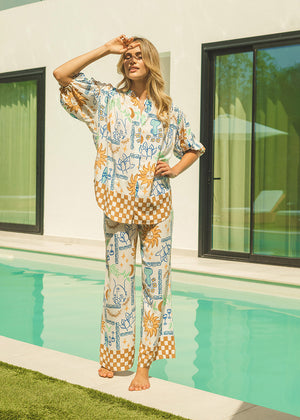 A person standing by a pool wearing a colorful floral wide-leg pantsuit with a drawstring waist and pockets at the hip.