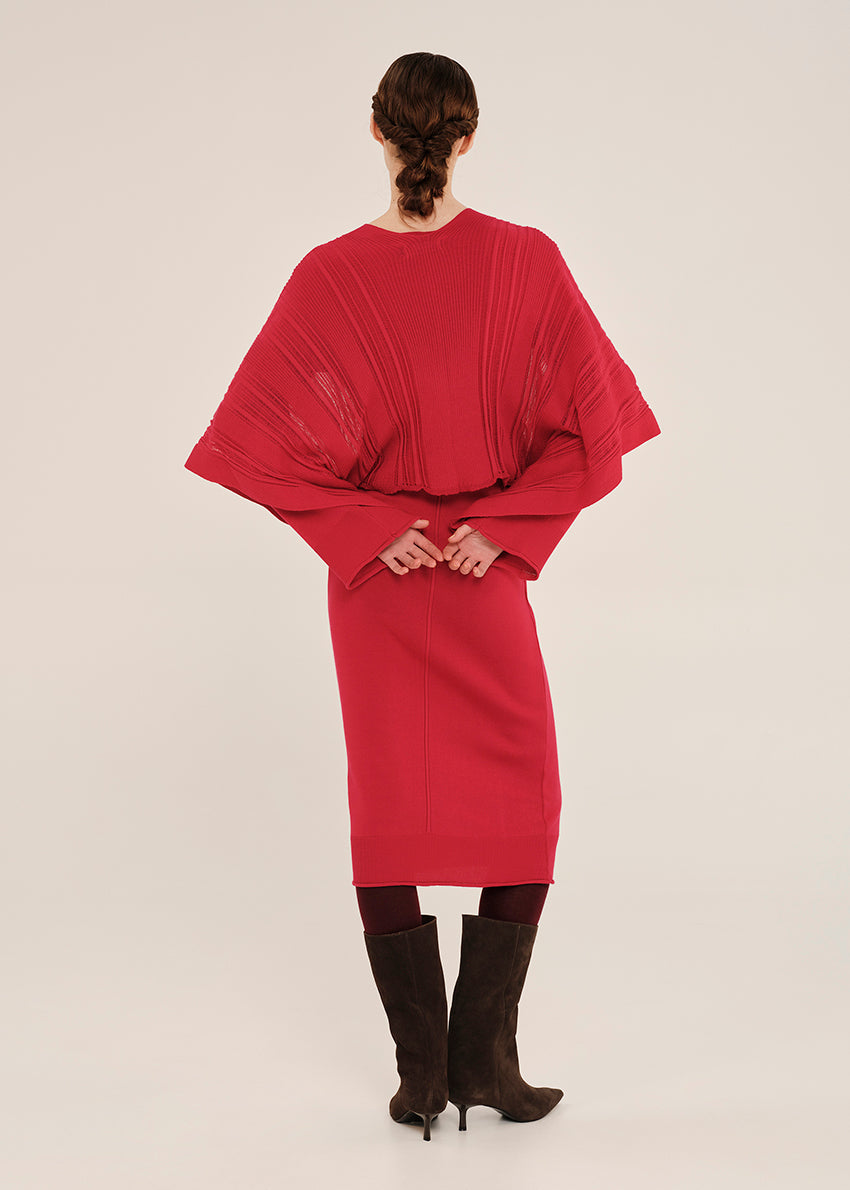 Person wearing a red dress with cape-like sleeves on a white background