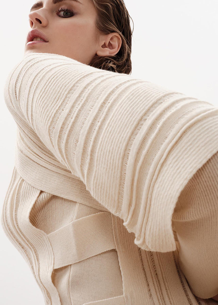 Close-up of a person wearing a beige ribbed sweater with a blurred background