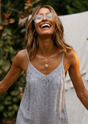Woman wearing a blue jumper and gold sunglasses with a blurred green background