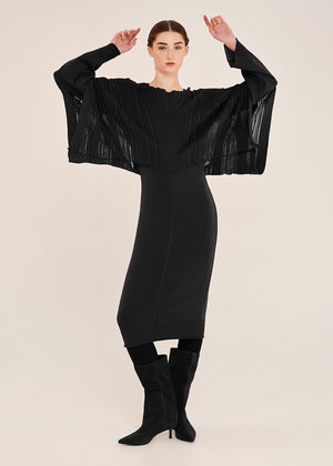 Woman wearing a black dress with sheer sleeves on a beige background