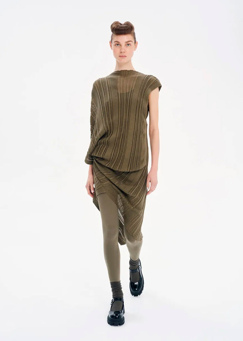 A model wearing a green knitted midi dress with asymmetrical shape and rib pattern, sleeveless on one side and short sleeved on the other, paired with black boots.