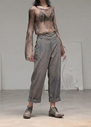 Person wearing a sheer top and gray pants in a minimalistic setting
