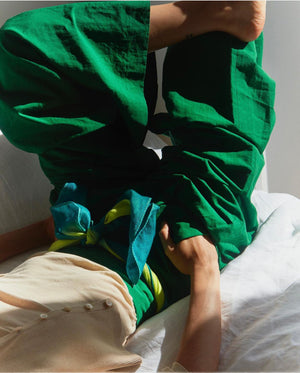 Person wearing green pants with a yellow belt, sitting on a bed.
