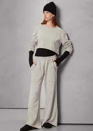 Person wearing a light gray cropped sweatshirt and light gray pants on a plain background