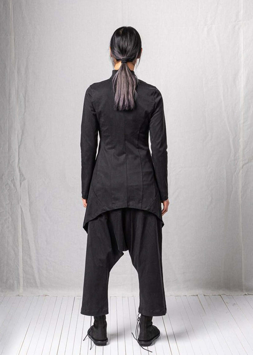 Person wearing a black outfit with an asymmetrical design against a plain background