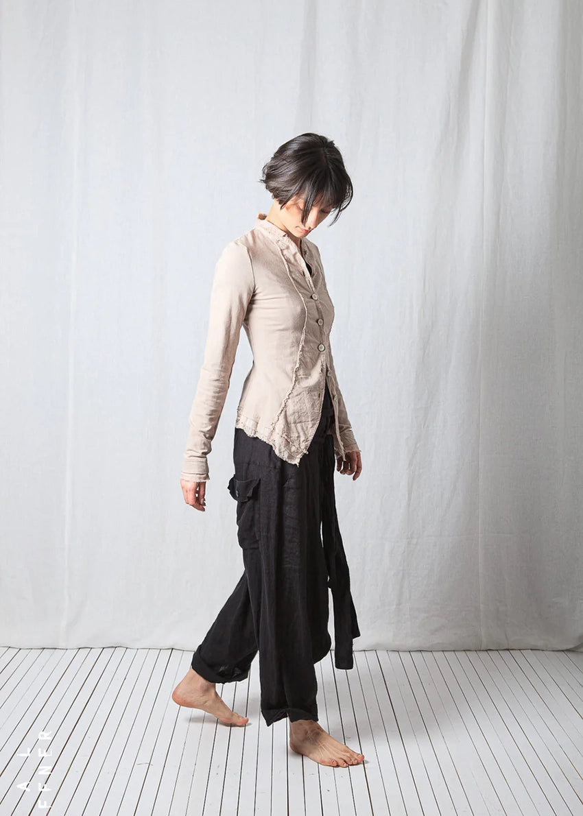 Person wearing a beige jacket and black pants standing against a white background