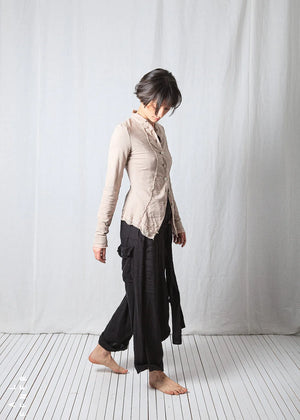 Person wearing a beige jacket and black pants standing against a white background