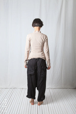 Person wearing a beige jacket and black pants standing against a white curtain.