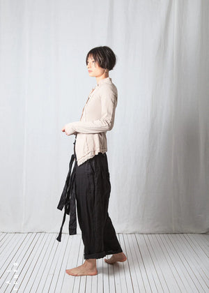 Person wearing a light-colored jacket and black pants standing against a plain white background