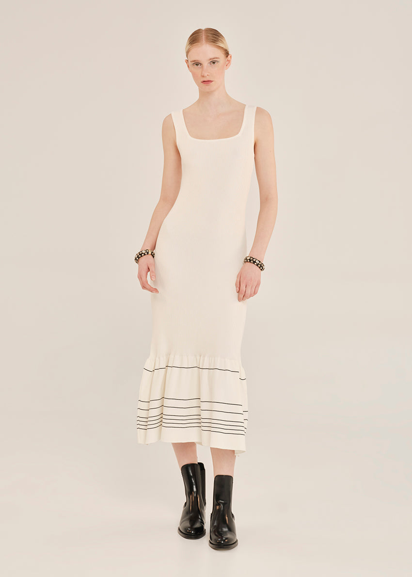 Woman wearing a white sleeveless dress with black trim on a plain background