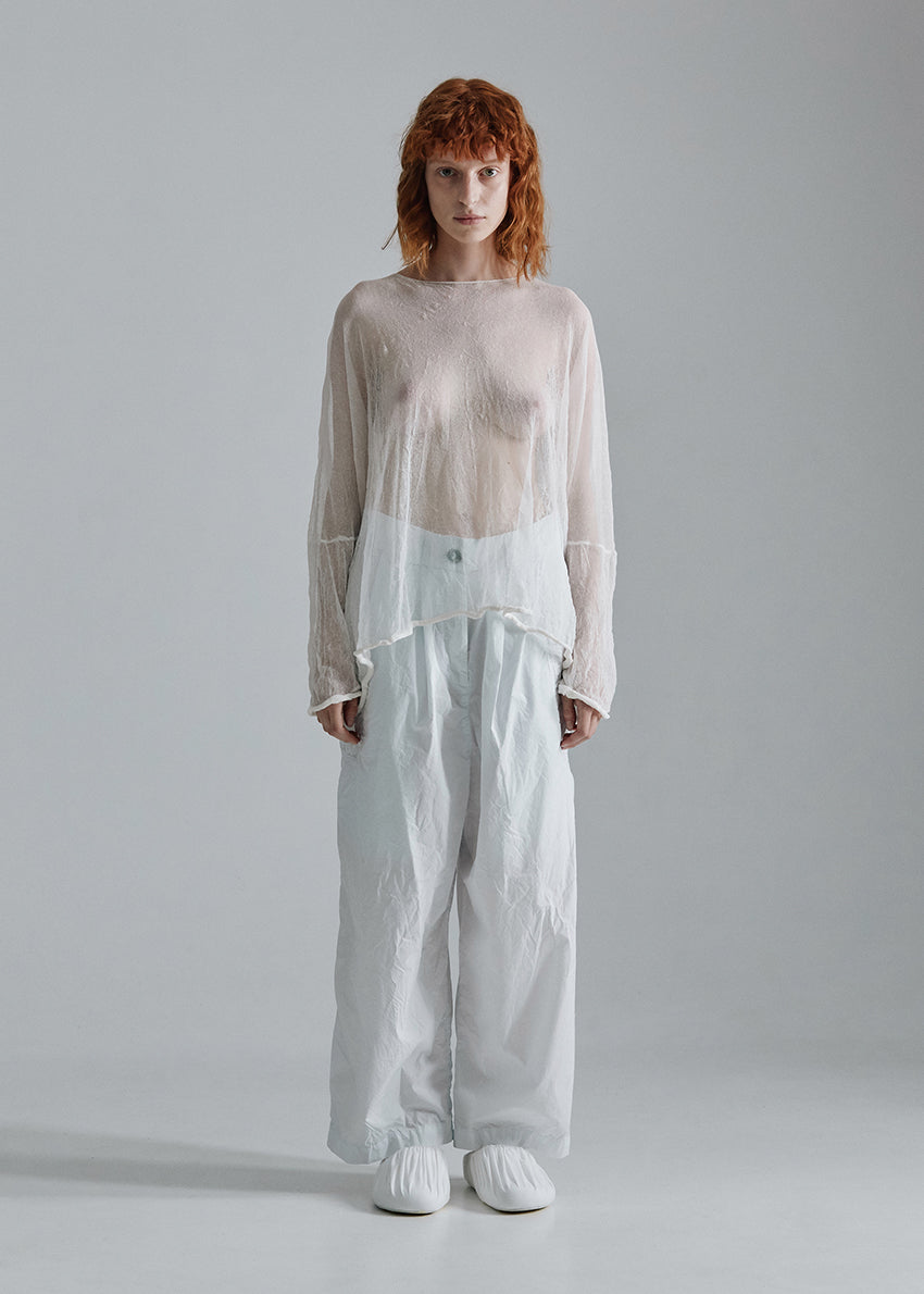 Person wearing a layered outfit with a sheer top and light pants on a plain background