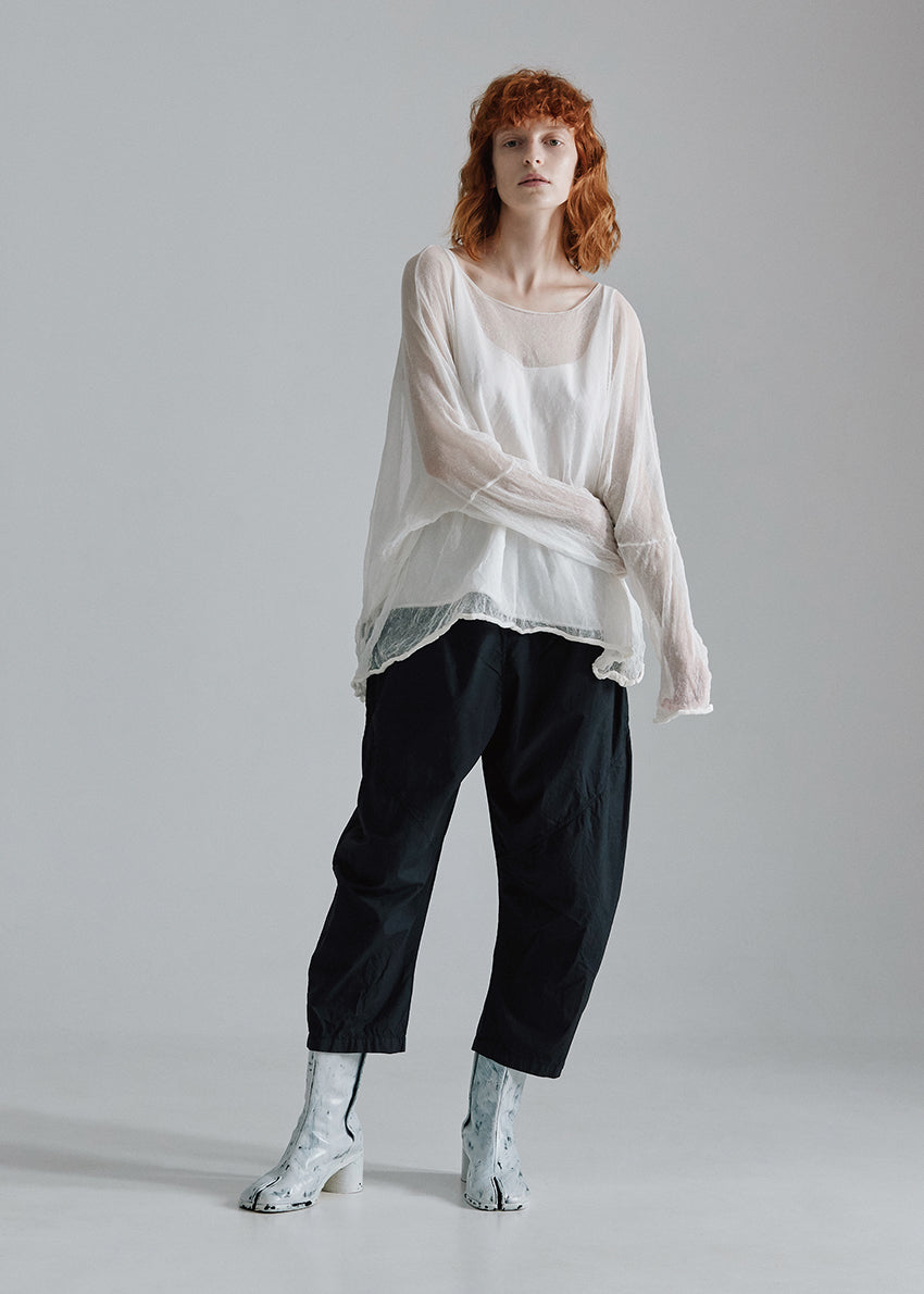 Woman wearing a loose-fitting white top and black pants on a plain background