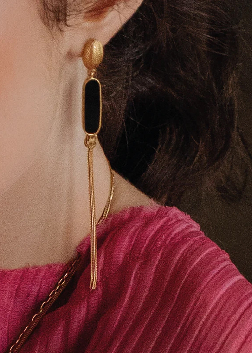 Gold and black earring worn by a person with dark hair and a pink top.