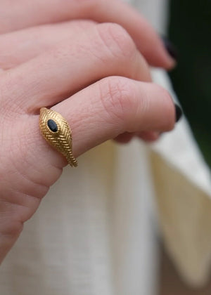 Gold ring with a black gemstone on a finger against a blurred background