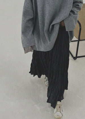 Person wearing a gray oversized sweater and black pleated skirt on a plain background