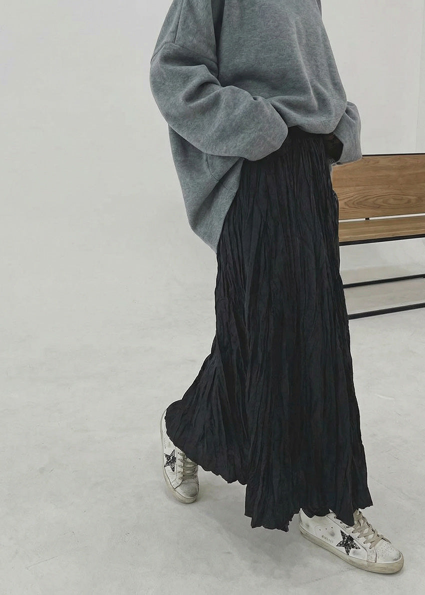 Person wearing a gray sweater and black pleated skirt with white sneakers on a light background