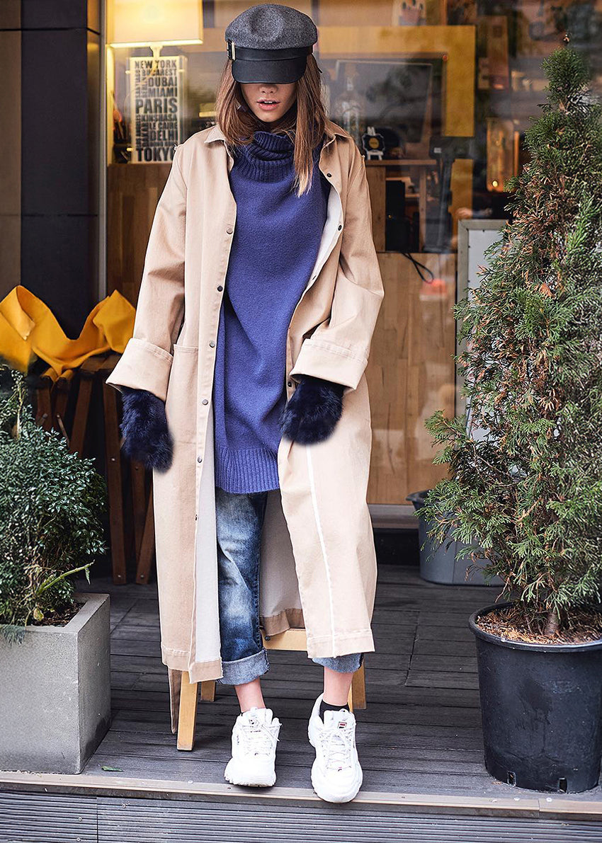 Person wearing a beige coat with a blue sweater and jeans on a shop entrance