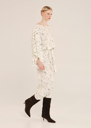 Woman wearing a white patterned dress with black boots on a plain background