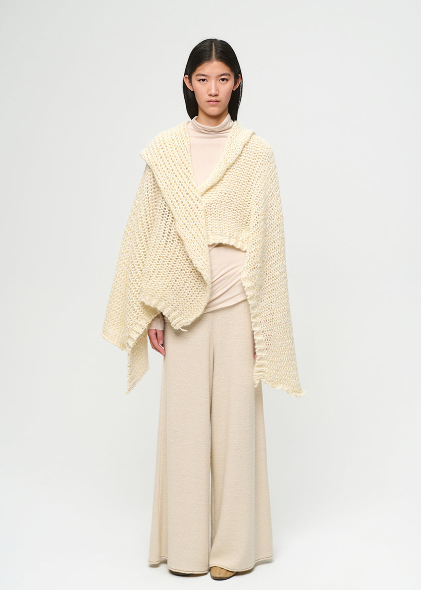 Woman wearing a beige knitted shawl over a beige outfit on a white background