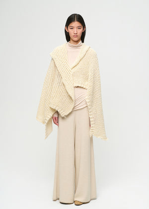 Woman wearing a beige knitted shawl over a beige outfit on a white background