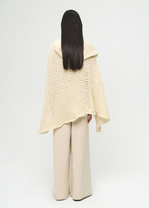 Person wearing a light beige knitted poncho and pants on a white background