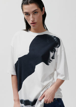 Model wearing a white t-shirt with a black graphic design on a plain background