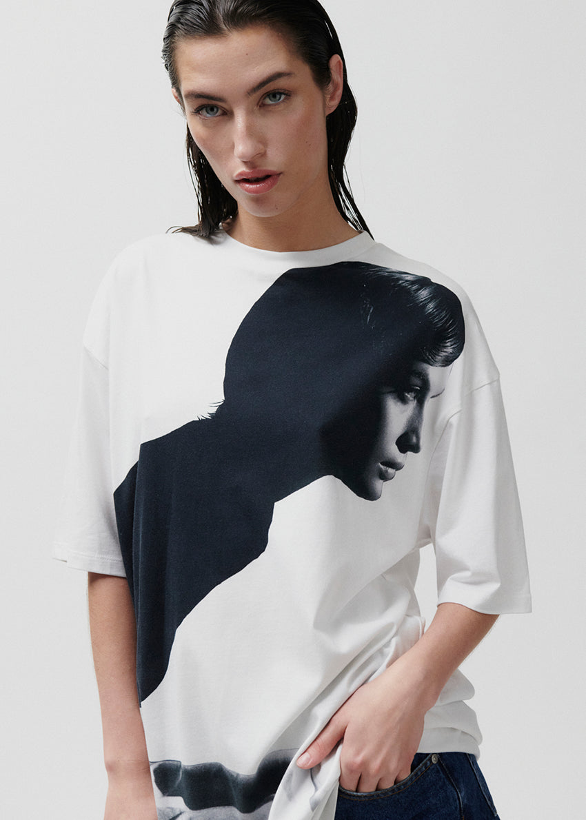 Model wearing a white t-shirt with a black graphic design on a plain background