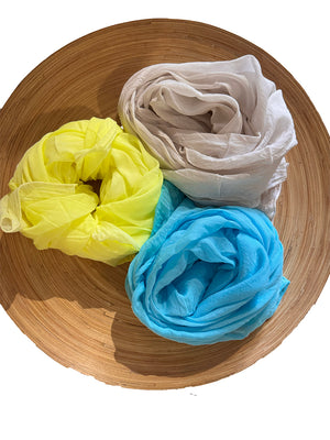 Three scarves in yellow, wheat, and blue on a wooden plate.